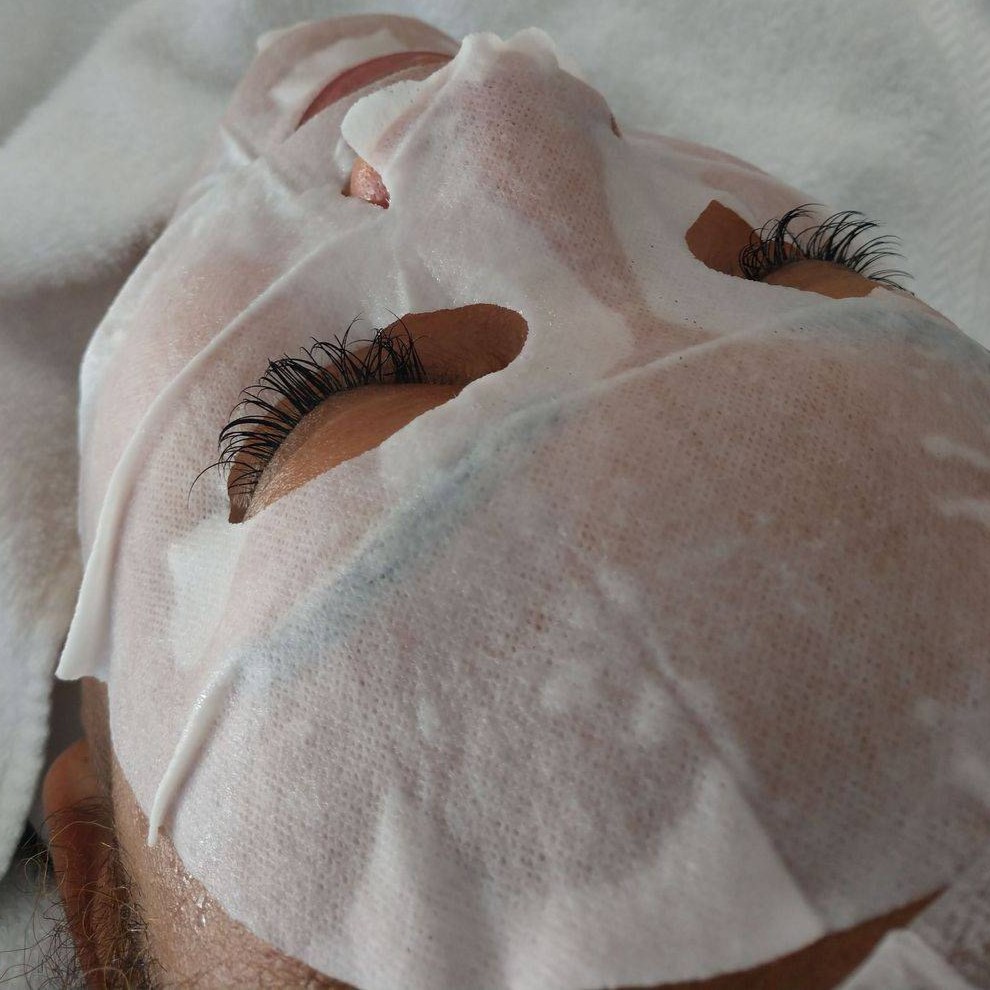 Guest wearing a hydrating sheet mask with lash extensions in place